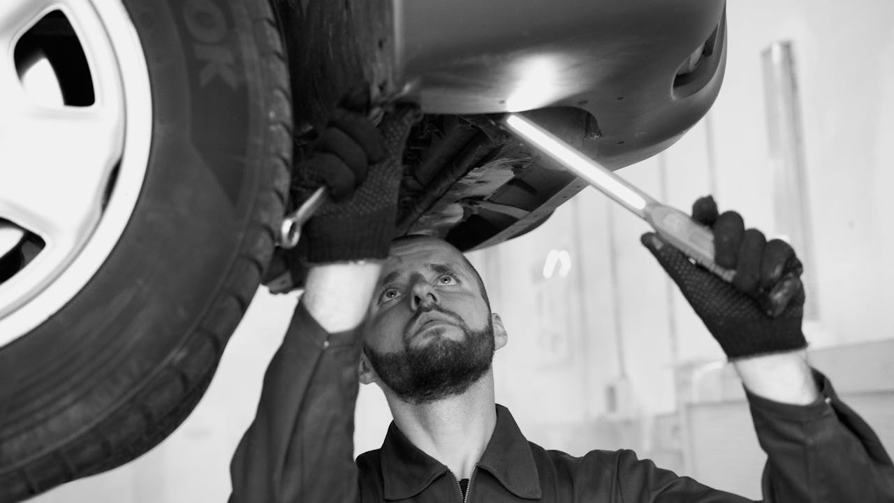 A mechanic inspects a cars underbody in a workshop, showcasing repair skills.